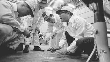 Soičiro Honda a niekoľko pracovníkov továrne v bielych kombinézach.